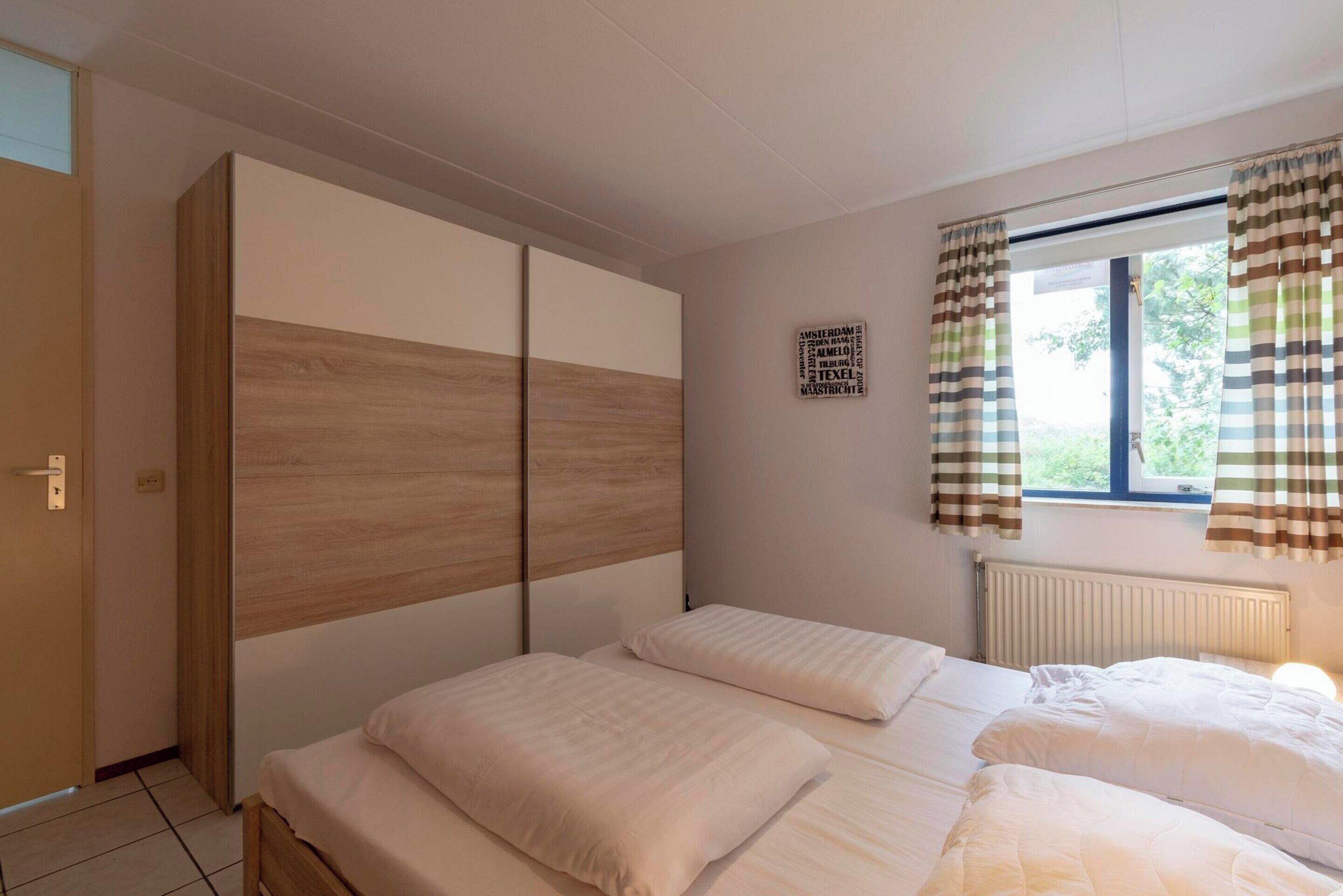 Une chambre avec deux lits, une armoire, une fenêtre avec des rideaux et un mur orné d’une enseigne.