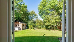 Une vue à travers une porte ouverte, donnant sur une cour arrière avec une pelouse, des arbres et un petit bâtiment.