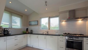 A modern kitchen with white cabinets, a black countertop, and stainless steel appliances including a stove and oven. - Holiday Home Sint Maartenszee Near Beach (Sint Maartensvlotbrug)