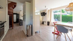 A modern kitchen with a built-in oven, a dining area with a table and chairs, and a large window offering a view of the garden. - Holiday Home Sint Maartenszee Near Beach (Sint Maartensvlotbrug)