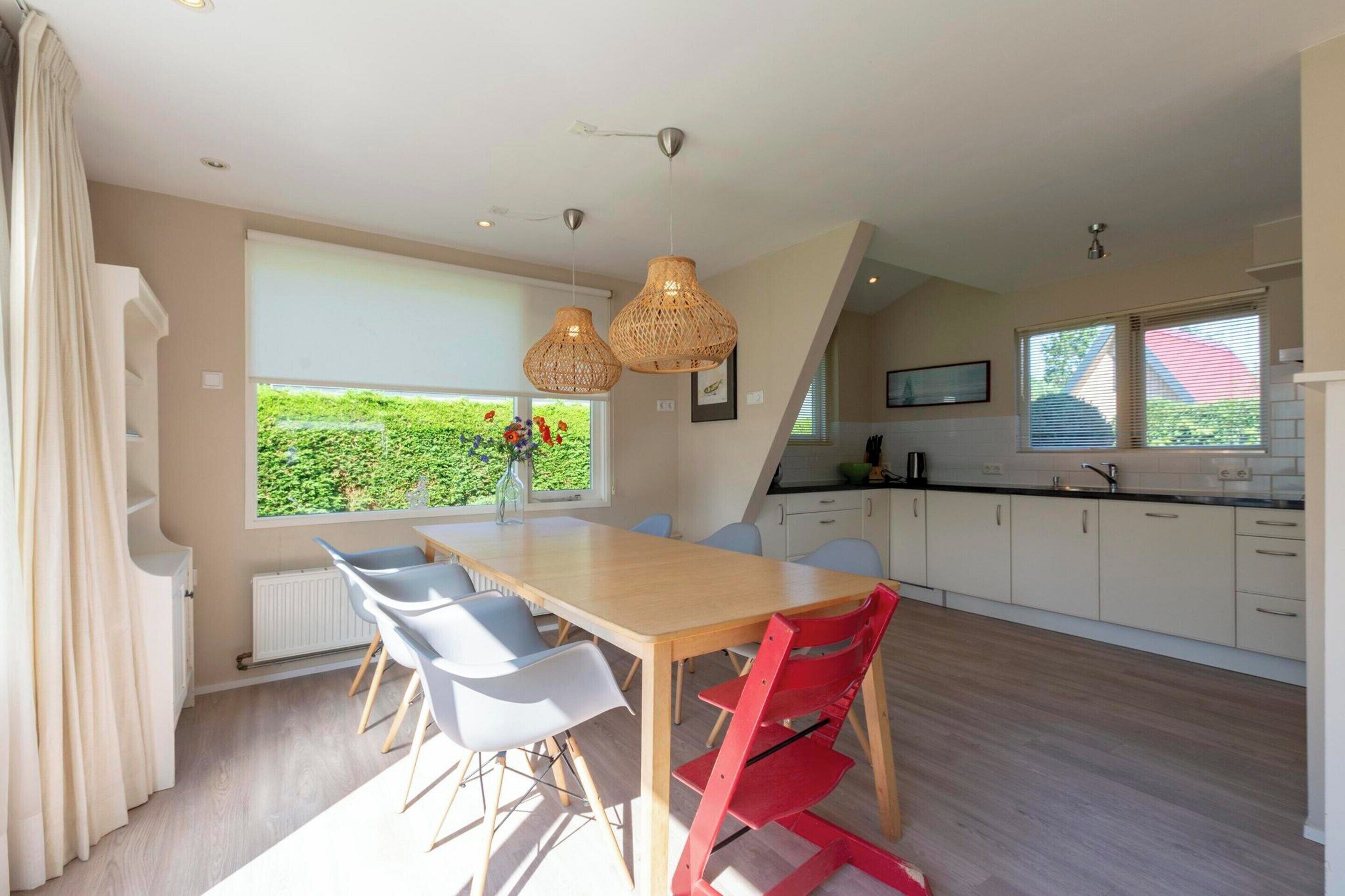 Cozinha moderna com área de refeições, destacando uma mesa e cadeiras de madeira, uma janela ampla com vista para o verde e luminárias pendentes.