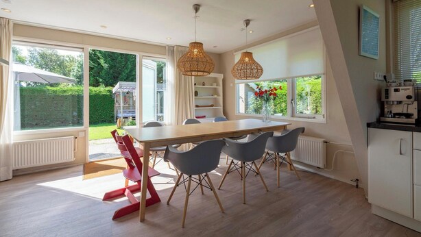 A modern kitchen with a large island, white cabinetry, and a view of the garden. - Holiday Home Sint Maartenszee Near Beach (Sint Maartensvlotbrug)