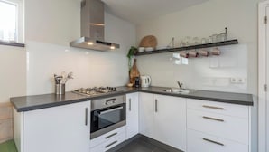 Une cuisine moderne avec des armoires blanches, une cuisinière à gaz, un four, une hotte en acier inoxydable et un évier encastré.
