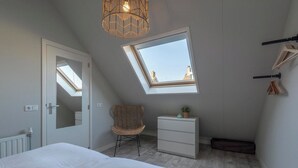 Une chambre avec un puits de lumière, un lit, une commode, une chaise et un radiateur.
