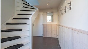Un escalier aux marches noires menant à une porte, un mur recouvert de panneaux en bois et un miroir accroché au mur.
