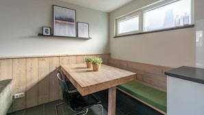 Une petite cuisine moderne, avec une table en bois, un banc et une fenêtre dotée d’étagères.