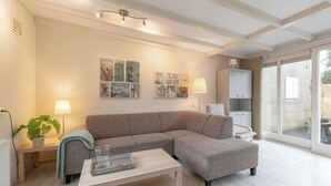 A modern living room with a sectional sofa, a small table, a lamp, and artwork on the wall. - Bungalow in Sint Maartenszee Near Beach (Sint Maartensvlotbrug)