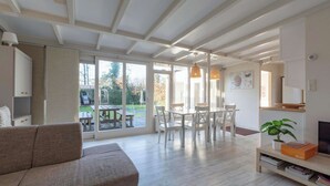 A modern living room with a sofa, dining table, chairs, and a TV. - Bungalow in Sint Maartenszee Near Beach (Sint Maartensvlotbrug)