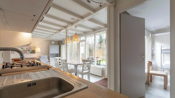 A modern kitchen with a large sink, wooden countertop, and a dining area with white chairs and a table. - Bungalow in Sint Maartenszee Near Beach (Sint Maartensvlotbrug)