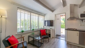 A modern kitchen with a built-in oven, a TV mounted above the counter, and a dining area with a glass table and chairs. - Holiday Home in Callantsoog Near Beach (Callantsoog)