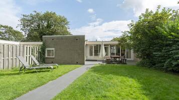A backyard with a brick building, a lawn, a concrete path, and outdoor furniture.