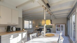 Eine moderne Küche mit weißen Schränken, einem Esstisch mit Stühlen und einem großen Fenster, das für natürliches Licht sorgt.