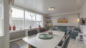 A modern living room with a dining table, grey sofas, and a painting on the wall. - Attractive Holiday Home With Garden (Sint Maartensvlotbrug)