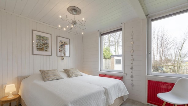 A bedroom with a bed, a nightstand, a chair, a window, and two framed pictures on the wall. - Attractive Holiday Home With Garden (Sint Maartensvlotbrug)