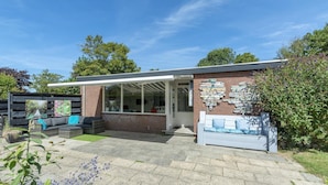 A modern house with a patio, outdoor seating, and a brick wall with artwork. - Attractive Holiday Home With Garden (Sint Maartensvlotbrug)