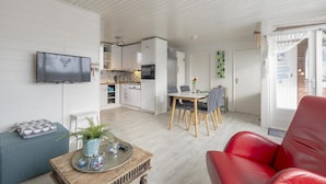 A modern living room with a flat-screen TV, a dining area with a table and chairs, a red leather sofa, and a kitchen in the background. - Attractive Holiday Home With Garden (Sint Maartensvlotbrug)