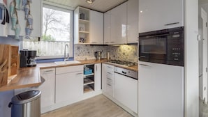 A modern kitchen with white cabinets, a built-in oven, and a coffee maker. - Attractive Holiday Home With Garden (Sint Maartensvlotbrug)