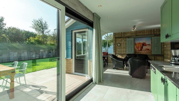 Een moderne keuken met groene kastjes, een eethoek met tafel en stoelen, en een schuifdeur naar een terras met een gazon en stoelen.
