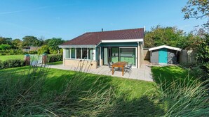 Een modern huis met een terras, een eettafel en een kleine schuur.