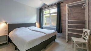 Een slaapkamer met een bed, nachtkastjes, een raam met gordijnen en een inbouwkast.