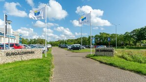 Een verhard pad dat leidt naar een bungalowpark met vlaggen, een stenen muur en een bord met de tekst 'DE GARNEKUJL'.