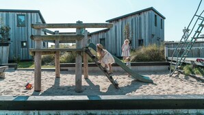 Ein Spielplatz mit Rutsche und Klettergerüst, umgeben von Holzbauten.