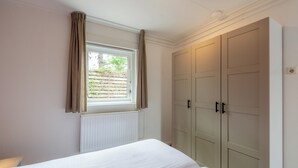 A bedroom with a bed, a window with curtains, a radiator, and a wardrobe. - Holiday Home Effe Sprage in Callanstoog Centre (Callantsoog)