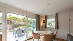 A modern interior with a round wooden table and four chairs, a sliding glass door leading to an outdoor patio, and a pendant light fixture. - Holiday Home Effe Sprage in Callanstoog Centre (Callantsoog)