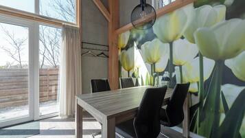A dining area with a wooden table, black chairs, a large floral mural, and a hanging light fixture.