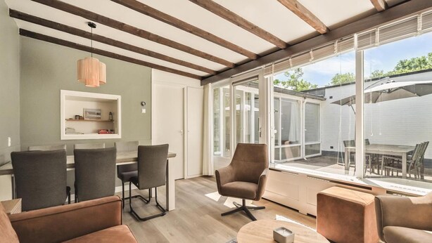 An open-plan living area with a dining table, chairs, sofas, and a large sliding glass door leading to an outdoor patio. - Duinland 197 Bungalow in Sint Maartenszee (Sint Maartensvlotbrug)