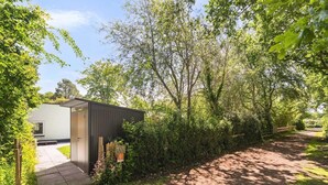 A pathway leading to a modern building with a door and a small garden area with flowers. - Duinland 197 Bungalow in Sint Maartenszee (Sint Maartensvlotbrug)