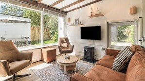 A modern living room with a fireplace, a flat-screen TV, and a large window overlooking a garden. - Duinland 197 Bungalow in Sint Maartenszee (Sint Maartensvlotbrug)