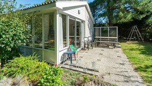 A covered outdoor area with a bench and chairs, surrounded by greenery and trees. - Family Home by the Dunes (Sint Maartensvlotbrug)