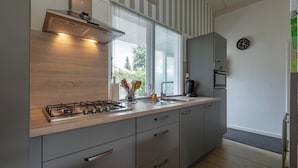 A modern kitchen with a gas stove, stainless steel appliances, and a window with blinds. - Family Home by the Dunes (Sint Maartensvlotbrug)
