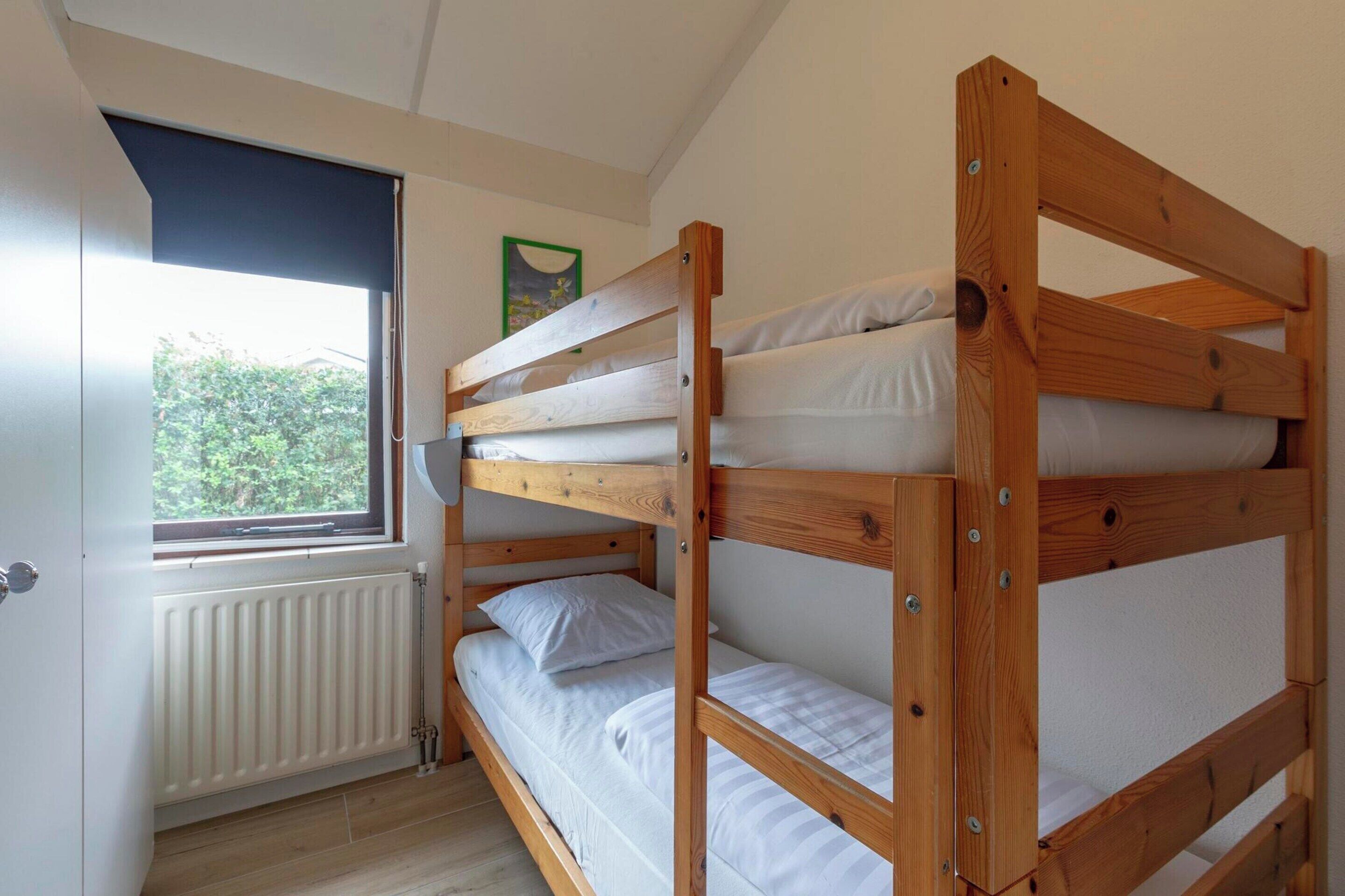 A bunk bed room with a window, radiator, and a framed picture on the wall.