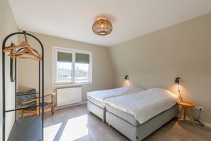 Un dormitorio con cama, una silla, un perchero, una ventana y una lámpara fijada a la pared.