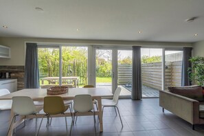 Un comedor moderno con una mesa grande y sillas, un sofá, y vistas a un jardín a través de puertas correderas amplias.