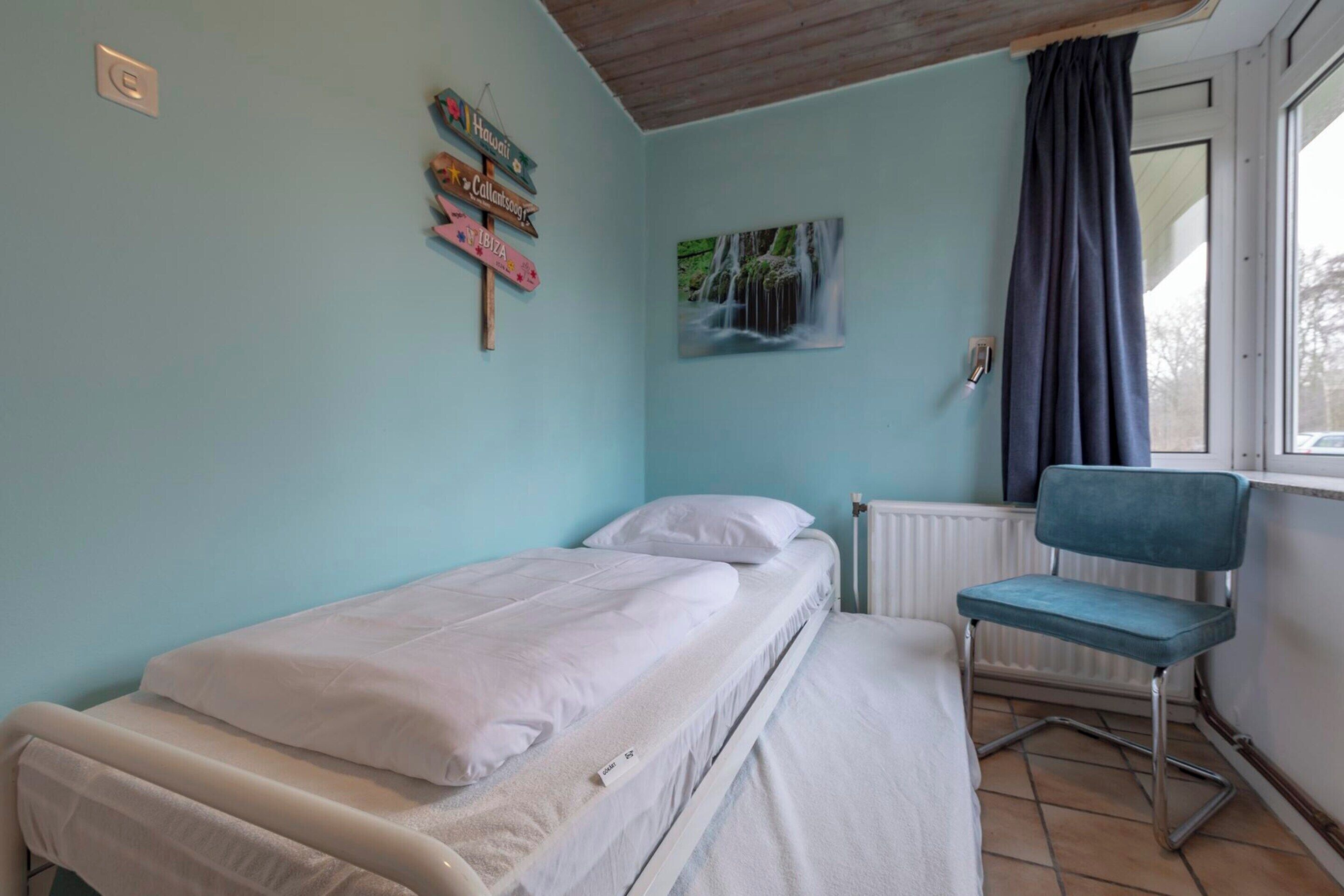 A single-bed room with a window, a chair, and a wall with signs.