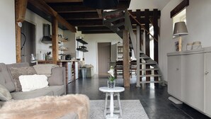 Un amplio salón con techo alto, una escalera y una cocina al fondo.