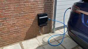A brick wall with an EV hub charging station and a blue charging cable connected to a car. - Bungalow With Sauna and Pool in Quiet Location (Sint Maartensvlotbrug)