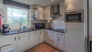 A modern kitchen with white cabinets, a microwave, a stove, and a sink. - Bungalow With Sauna and Pool in Quiet Location (Sint Maartensvlotbrug)