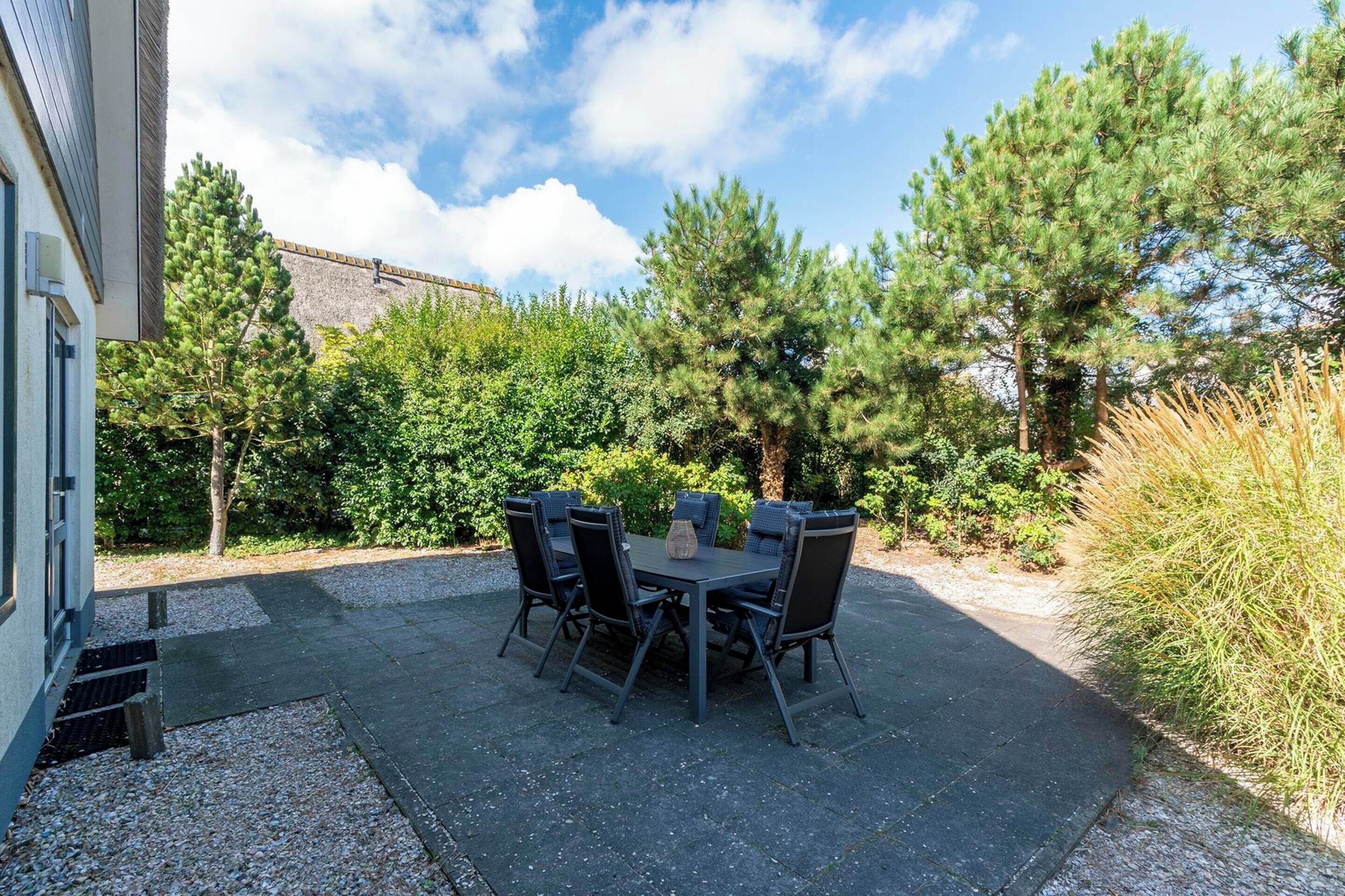 An outdoor patio with a table and chairs, surrounded by trees and a building.