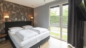 A modern bedroom with a large bed, two bedside lamps, and a sliding glass door leading to a balcony. - Spacious Bunglow With Garden (Sint Maartensvlotbrug)