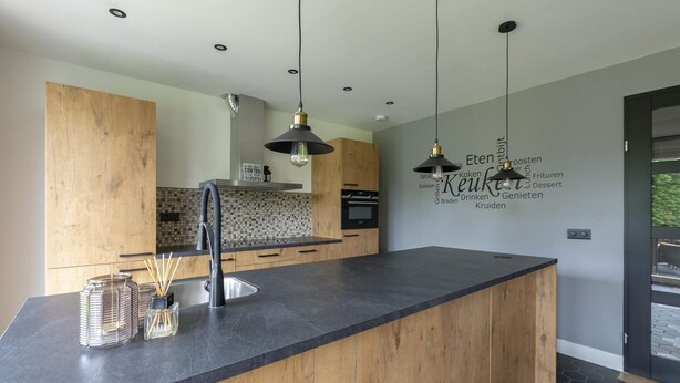 A modern kitchen with a central island, wooden cabinets, and pendant lighting. - Spacious Bunglow With Garden (Sint Maartensvlotbrug)