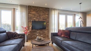 A modern living room with a stone wall, two sofas, a coffee table, and a flat-screen TV. - Spacious Bunglow With Garden (Sint Maartensvlotbrug)