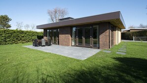 A modern house with a patio, a dining area, and a well-maintained lawn. - Spacious Bunglow With Garden (Sint Maartensvlotbrug)