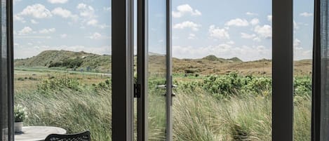A view from a room with a sliding glass door to a landscape with hills and vegetation.