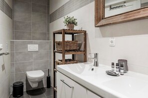 A bathroom with a white sink, a mirror, a toilet, and a shelf with baskets and a potted plant. - Seaside Double Duyn Suites (Callantsoog)