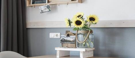 A room with a table, a hanging lamp, a shelf with a picture frame, and a vase with sunflowers.