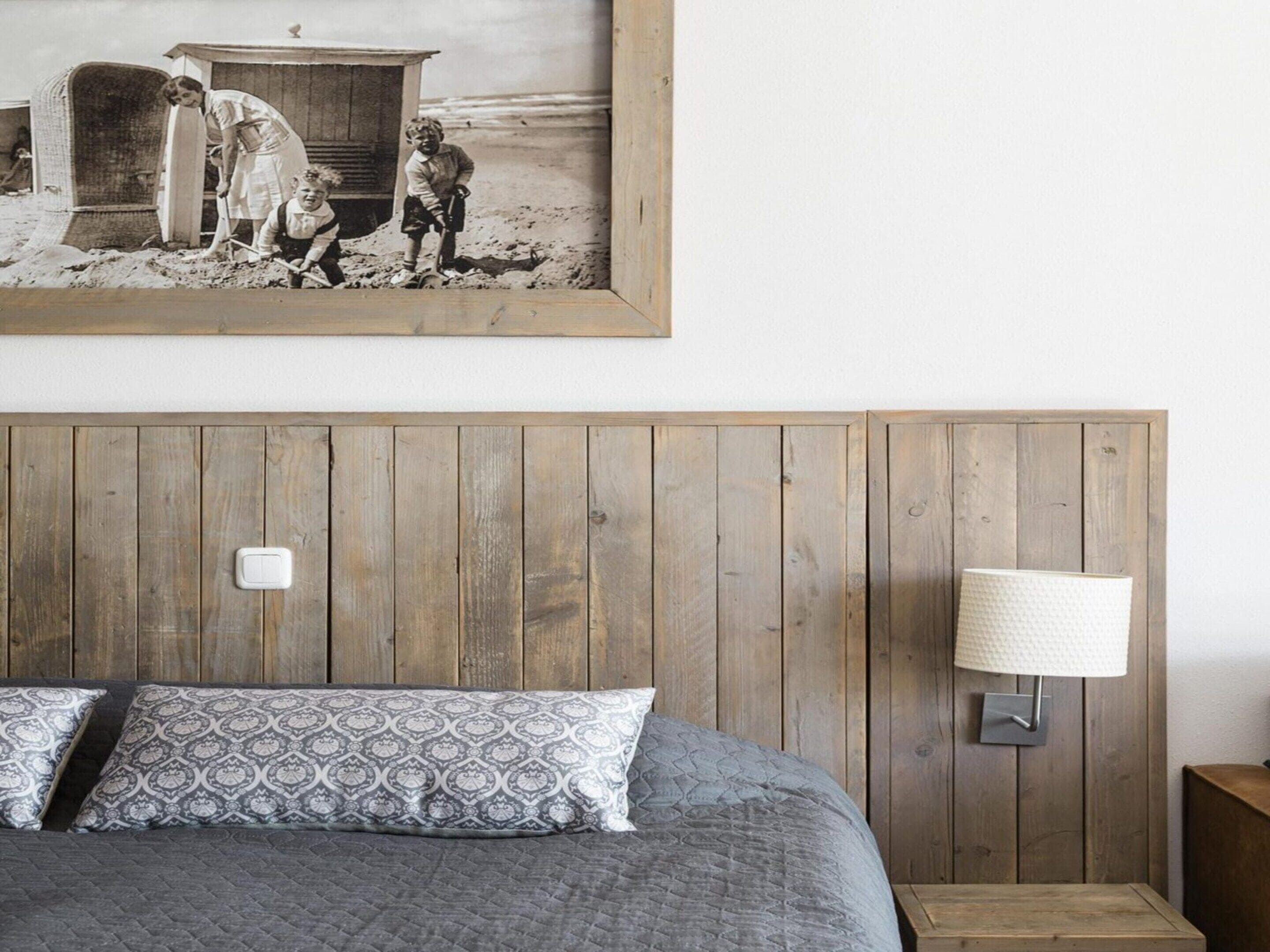 A bedroom with a wooden headboard, a bed with patterned pillows, a nightstand, and a wall-mounted lamp.